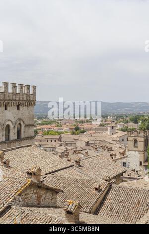 Vue sur les toits ocres descendant en cascade vers les collines lointaines, surveillées par la forteresse en pierre vieillie sous un ciel doux et nuageux, Gubbio, Ombrie, Italie. Banque D'Images
