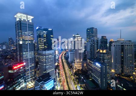 Vue aérienne nocturne du quartier central des affaires de Jakarta, avec gratte-ciel illuminés et feux de circulation animés le long d'une avenue principale. Banque D'Images