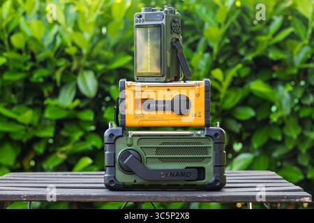 VINKOVCI, CROATIE, 06.13.2025:trois radios portatives avec panneaux solaires présentées à l'extérieur sur une surface en bois sur un fond vert naturel. Perfe Banque D'Images