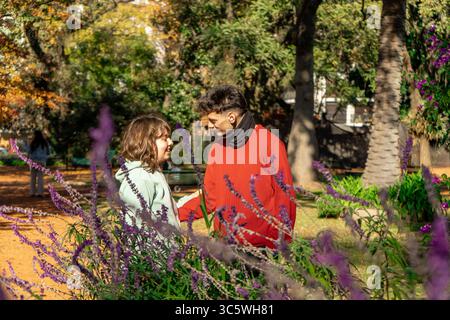 Jeune couple profite d'un moment romantique ensemble, se tenant la main et parlant au milieu de fleurs violettes en fleurs dans un parc Banque D'Images