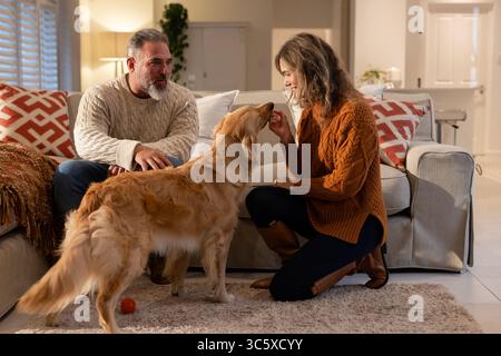 Couple assis sur le canapé, agenouillé sur un tapis en peluche offrant un régal à Golden retriever dans le salon Banque D'Images