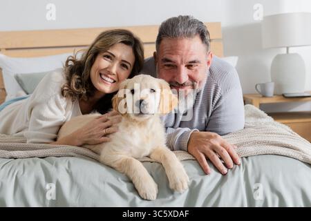 Couple allongé sur l'estomac sur le lit caressant Golden retriever chiot près de la lampe de table de nuit dans la chambre Banque D'Images
