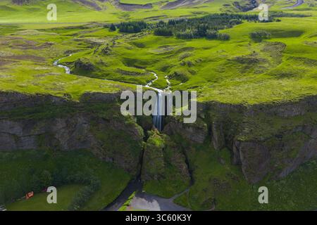 Vue aérienne d'une cascade dans une gorge avec un terrain vert luxuriant en Islande Banque D'Images