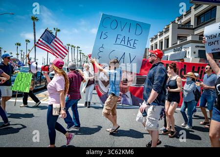 9 mai 2020, Huntington Beach, Californie, États-Unis : un homme tient une pancarte disant qu'il croit que COVID-19 est "FAUX et GAY", alors que d'autres manifestants de quarantaine portent une bannière montrant le gouverneur de l'État fait pour ressembler à Adolf Hitler. En blanc, le militant de droite Leigh Dundas dirige le groupe. Lors d'une manifestation contre la réouverture de la Californie, près de la jetée de Huntington Beach. (Crédit image : © Orin Louis/ZUMA Wire) Banque D'Images