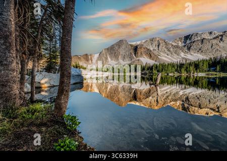 Encadrée par la forêt, cette photo tranquille du lac Mirror dans le Wyoming capture le reflet limpide de la chaîne des neiges sous des nuages pastel. Le morni Banque D'Images
