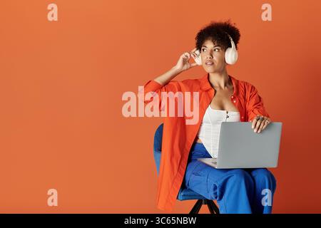 Une femme afro-américaine aux cheveux bouclés dans une tenue élégante s'engage avec son ordinateur portable dans un studio lumineux. Banque D'Images