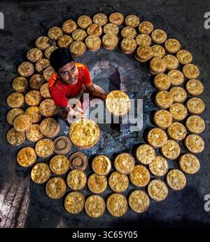 Bogura, Bangladesh - 03 mai 2020 : vue d'un boulanger, baigné de lumière chaude, expose des produits fraîchement cuits, entourés d'un anneau de friandises brun doré, mettant en valeur les textures et les tons de la boulangerie. Banque D'Images