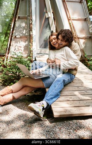 Couple aimant assis ensemble sur un banc en bois, partageant des moments joyeux et des rires dans un parc luxuriant. Banque D'Images