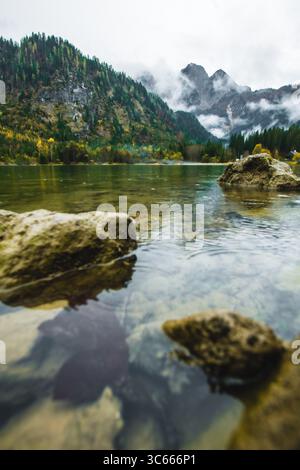 Vue sur le lac serein de Gousausee reflétant les Alpes majestueuses sous un ciel nuageux, avec des rochers émergeant des eaux cristallines, Gousau, Autriche. Banque D'Images