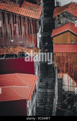 Porto, Portugal - 17 juin 2022 : vue sur un escalier étroit et abrupt traversant la vieille ville, flanqué de bâtiments aux toits en terre cuite et aux murs altérés. Banque D'Images