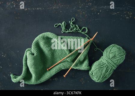 Projet de tricot avec de la laine verte et des aiguilles de bambou sur fond rustique. Projet de tricot incomplet avec des aiguilles en bois. Banque D'Images
