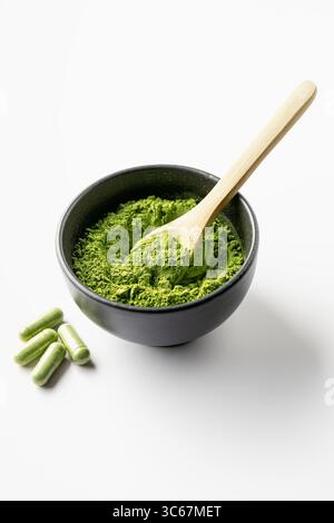 Poudre de feuilles de moringa dans un petit bol et capsules de moringa sur fond blanc. Banque D'Images