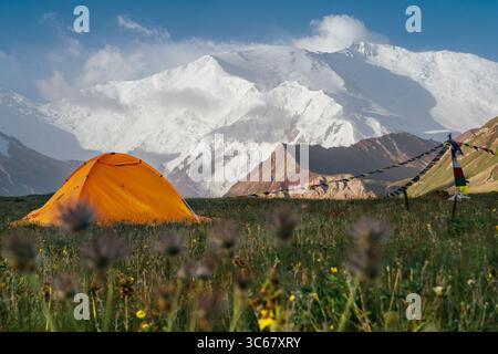 Tente jaune vif se tient seul sur l'herbe verte à 3600m Camp de base avec une vaste vue panoramique sur les montagnes du Pamir avec le pic Lénine. Concept de personnes actives. Banque D'Images
