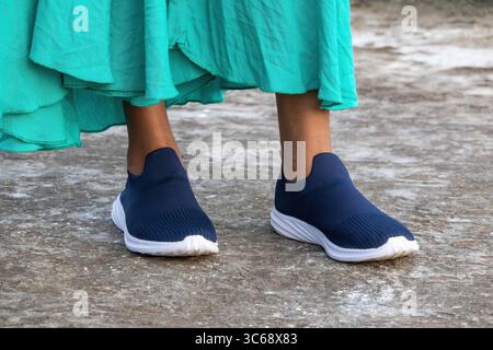 Jambes de femme avec une paire de baskets à enfiler. Gros plan des jambes d'une fille bengali portant des chaussures, se tient sur un sol en béton. Banque D'Images