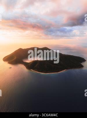 Vue aérienne du lac de cratère volcanique de Satonda Island scintille sous un ciel pastel, ses eaux sombres contrastant avec la lumière dorée, Satonda Island, D. Banque D'Images
