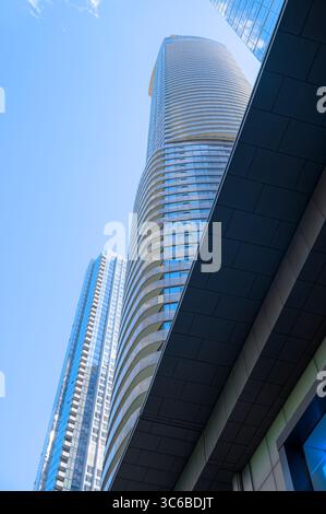 Une tour moderne aux balcons en verre incurvés s'élève dans le ciel, encadrée par une architecture angulaire et des tours environnantes. Banque D'Images
