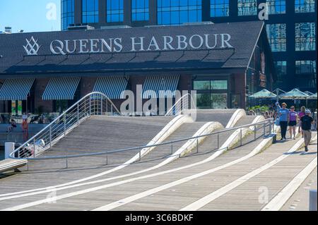 Les gens marchent à côté du bâtiment Queens Harbour près d'une promenade en forme de vague au bord de l'eau. Banque D'Images