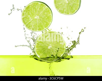 Citrons verts frais tombant dans la boisson éclaboussante sur fond blanc Banque D'Images