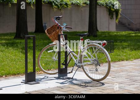 Vélo garé au porte-vélos sur le trottoir. Vélo rétro avec panier en osier Banque D'Images