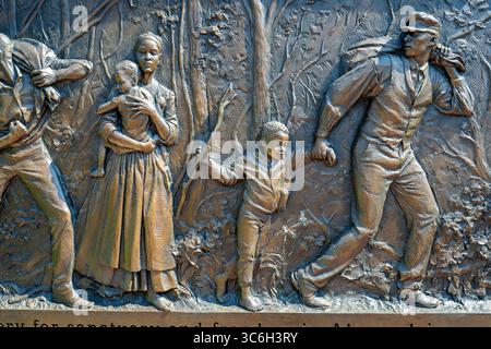 ALEXANDRIA, Virginie — Une sculpture en relief en bronze représente une famille fuyant l'esclavage au mémorial du cimetière des Contrabands et des Freedmen, avec l'inscription « fuir l'esclavage pour un sanctuaire et la liberté à Alexandrie ». L'œuvre du sculpteur local Joanna Blake fait partie du mémorial dédié en 2014 à 1 711 Afro-Américains morts entre 1864-1869 et enterrés dans le cimetière historique. Le cimetière est établi en mars 1864 sur des terres confédérées confisquées pour servir la communauté de contrebande et d'affranchis d'Alexandrie pendant la guerre de Sécession. Le site a acquis une importance nationale à Decemb Banque D'Images