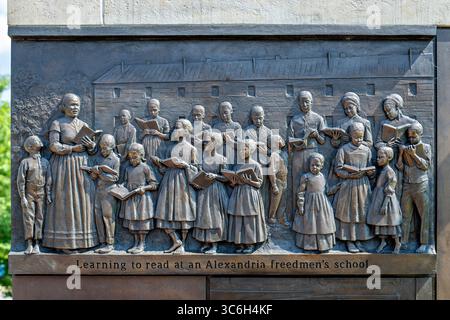 ALEXANDRIA, Virginie — Une sculpture en relief en bronze représentant des enfants apprenant à lire dans une école d'affranchis d'Alexandrie fait partie du mémorial du cimetière des Contrabands et des affranchis, dédié en 2014. Le relief, créé par la sculptrice locale Joanna Blake, illustre les initiatives éducatives qui ont émergé au sein de la communauté afro-américaine d'Alexandrie pendant la guerre de Sécession, où les écoles de contrebande ont atteint des taux de participation remarquables avec 400 enfants fréquentant des classes quotidiennes en 1864. Le mémorial commémore 1 711 Afro-Américains documentés morts entre 1864-1869 et enterrés dans le cemet Banque D'Images