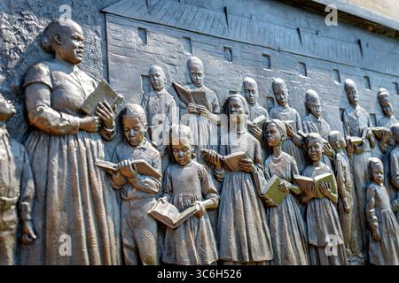 ALEXANDRIA, Virginie — Une sculpture en relief en bronze représentant des enfants apprenant à lire dans une école d'affranchis d'Alexandrie fait partie du mémorial du cimetière des Contrabands et des affranchis, dédié en 2014. Le relief, créé par la sculptrice locale Joanna Blake, illustre les initiatives éducatives qui ont émergé au sein de la communauté afro-américaine d'Alexandrie pendant la guerre de Sécession, où les écoles de contrebande ont atteint des taux de participation remarquables avec 400 enfants fréquentant des classes quotidiennes en 1864. Le mémorial commémore 1 711 Afro-Américains documentés morts entre 1864-1869 et enterrés dans le cemet Banque D'Images