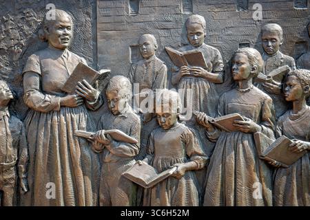 ALEXANDRIA, Virginie — Une sculpture en relief en bronze représentant des enfants apprenant à lire dans une école d'affranchis d'Alexandrie fait partie du mémorial du cimetière des Contrabands et des affranchis, dédié en 2014. Le relief, créé par la sculptrice locale Joanna Blake, illustre les initiatives éducatives qui ont émergé au sein de la communauté afro-américaine d'Alexandrie pendant la guerre de Sécession, où les écoles de contrebande ont atteint des taux de participation remarquables avec 400 enfants fréquentant des classes quotidiennes en 1864. Le mémorial commémore 1 711 Afro-Américains documentés morts entre 1864-1869 et enterrés dans le cemet Banque D'Images
