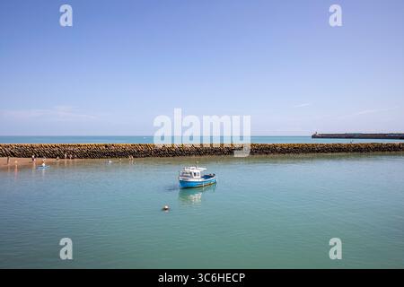 Petit bateau de pêche unique dans le port de Folkestone par une journée d'été ensoleillée avec un ciel bleu et de l'eau verte. Avec la belle digue derrière. Banque D'Images