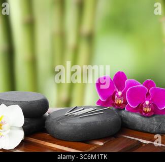 Aiguilles d'acupuncture, pierres de spa et fleurs sur table en bois à l'extérieur Banque D'Images