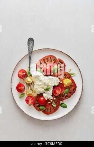 Salade Caprese avec tranches de tomates mûres, fromage burrata crémeux, pignons de pin et feuilles de basilic frais sur fond clair, vue de dessus Banque D'Images