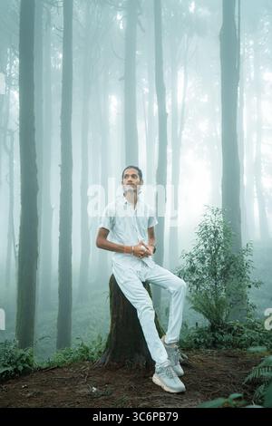 Autoportrait d'un homme assis sur une souche d'arbre dans une forêt brumeuse à Darjeeling, en Inde. Capturé pendant la saison de la mousson avec filtrage de lumière douce. Banque D'Images