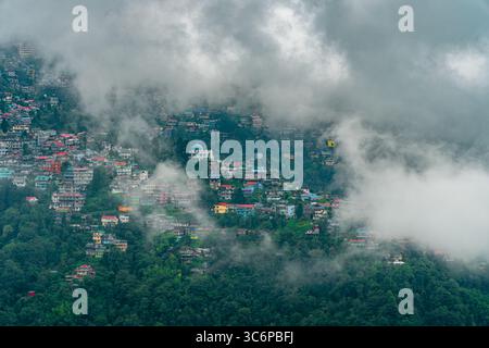 Mousson brumeuse vue matinale de Darjeeling, une station de colline célèbre dans le Bengale occidental, Inde. Des nuages denses planent au-dessus de maisons colorées à flanc de colline entourées. Banque D'Images