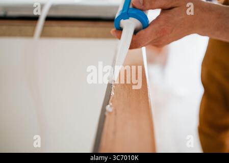 Travailleur de la construction appliquant un scellant silicone sur une planche de bois à l'aide d'un pistolet à calfeutrer, assurant l'étanchéité à l'air et à l'eau pendant les travaux de rénovation ou d'installation Banque D'Images