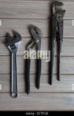Pose à plat haute résolution de trois outils à main métalliques — clé réglable, pince à joint coulissant et clé à tube — disposés sur une surface en bois rustique Banque D'Images