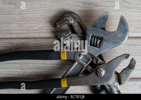 Un gros plan de diverses clés métalliques, y compris les types réglables, à tuyau et à joint coulissant, soigneusement disposées sur un établi en bois rustique Banque D'Images