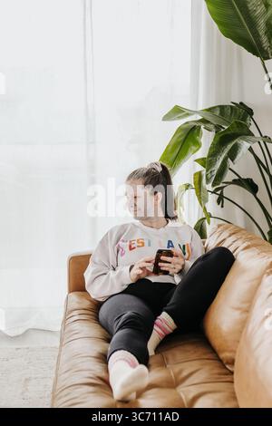 Femme d'âge moyen se détend sur le canapé tout en portant le masque d'argile au téléphone Banque D'Images