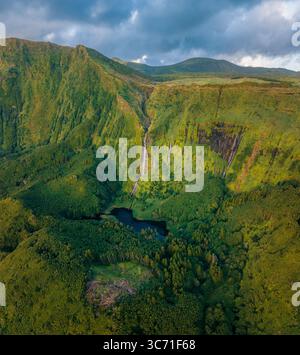 Vue aérienne des cascades plongez dans des falaises verdoyantes dans une piscine sombre et réfléchissante nichée au milieu d'une végétation luxuriante, Fajãzinha, Açores, Portugal. Banque D'Images