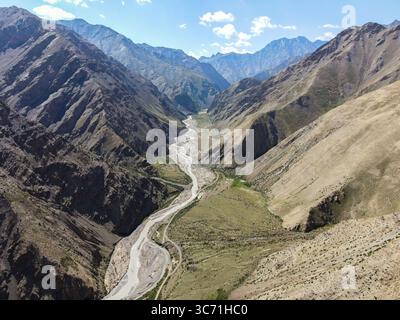 Une photo par drone d'une rivière étroite serpentant à travers un canyon profond et accidenté avec des parois rocheuses abruptes et des montagnes sous un ciel bleu Banque D'Images
