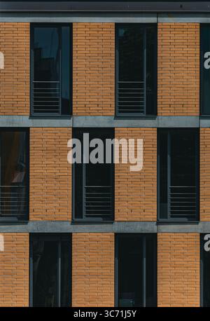 Vue de face d'un bâtiment urbain contemporain avec des murs en briques orange et de hautes fenêtres à cadre sombre dans un motif géométrique répétitif. Résidentiel moderne Banque D'Images