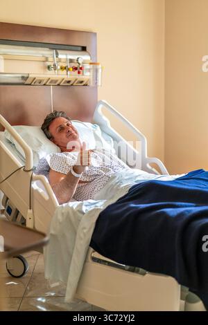 Patient heureux dans le lit d'hôpital donnant les pouces pour la guérison. Banque D'Images