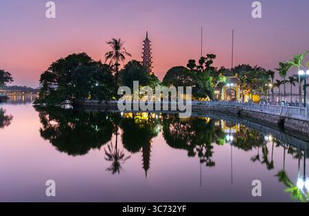Vue paisible de la pagode Tran Quoc se reflétant sur le lac à Hanoi, Vietnam, lors d'un coucher de soleil de teinte rose. Banque D'Images