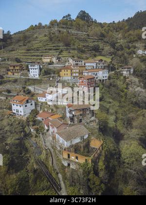 Vue aérienne de maisons groupées avec des toits en terre cuite accrochés à la colline verdoyante et abrupte, un village pittoresque niché dans l'étreinte de la nature, OS Peares, Ourense, Espagne. Banque D'Images