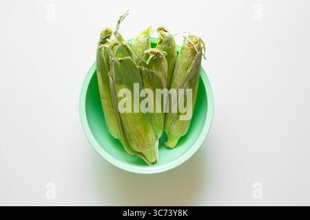 Épis de maïs frais en coque dans un bol en plastique vert sur fond blanc, légume, nourriture de ferme, isolé, vue de dessus Banque D'Images