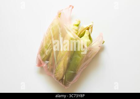 Épis de maïs en coque dans un sac en plastique transparent sur fond blanc, maïs frais pour la cuisson, récolte agricole, achat de légumes Banque D'Images