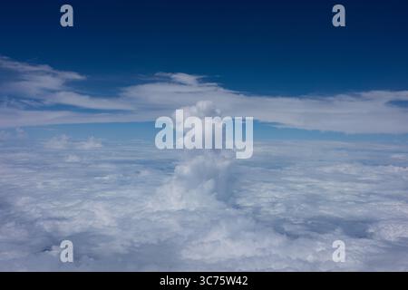 Une vue éthérée d'au-dessus des nuages, avec une formation de cumulus dense et imposante s'élevant d'une vaste couche de nuages mous en dessous. Banque D'Images