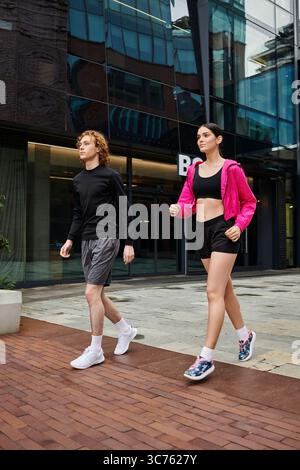 Deux jeunes sportifs marchent vigoureusement dans une ville moderne dans des vêtements de sport dynamiques. Banque D'Images