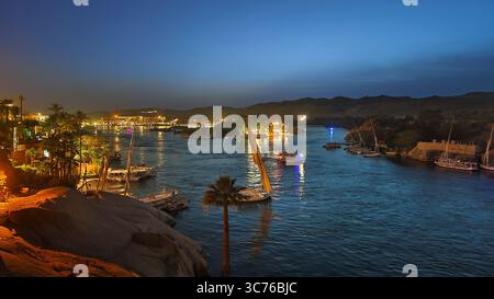 Felouques illuminées naviguant sur le nil la nuit, avec la ville d'Assouan en arrière-plan, Egypte Banque D'Images