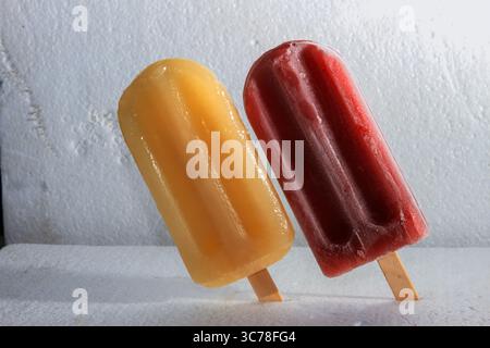 Deux popsicles traditionnelles vibrantes, l'une jaune et l'autre rouge, se dressent sur une surface texturée blanche, mettant en vedette un régal estival classique de la ville de New Taipei, Banque D'Images