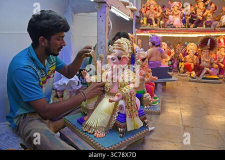 Un artisan décore l'idole du Dieu hindou à tête d'éléphant Ganesh pour la vente dans un atelier. Les artisans obtiennent les idoles du Dieu hindou à tête d'éléphant Ganesh prêtes à la vente car le festival de dix jours de Ganesh Chaturthi commencera du 27 août au 6 septembre qui sera célébré dans tout le pays. Banque D'Images