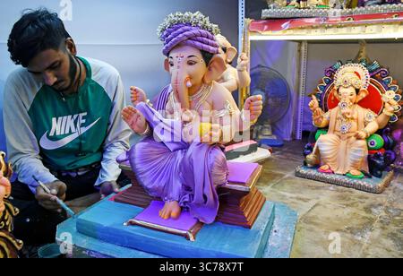 Un artisan peint l'idole du Dieu hindou à tête d'éléphant Ganesh pour la vente dans un atelier. Les artisans obtiennent les idoles du Dieu hindou à tête d'éléphant Ganesh prêtes à la vente car le festival de dix jours de Ganesh Chaturthi commencera du 27 août au 6 septembre qui sera célébré dans tout le pays. Banque D'Images